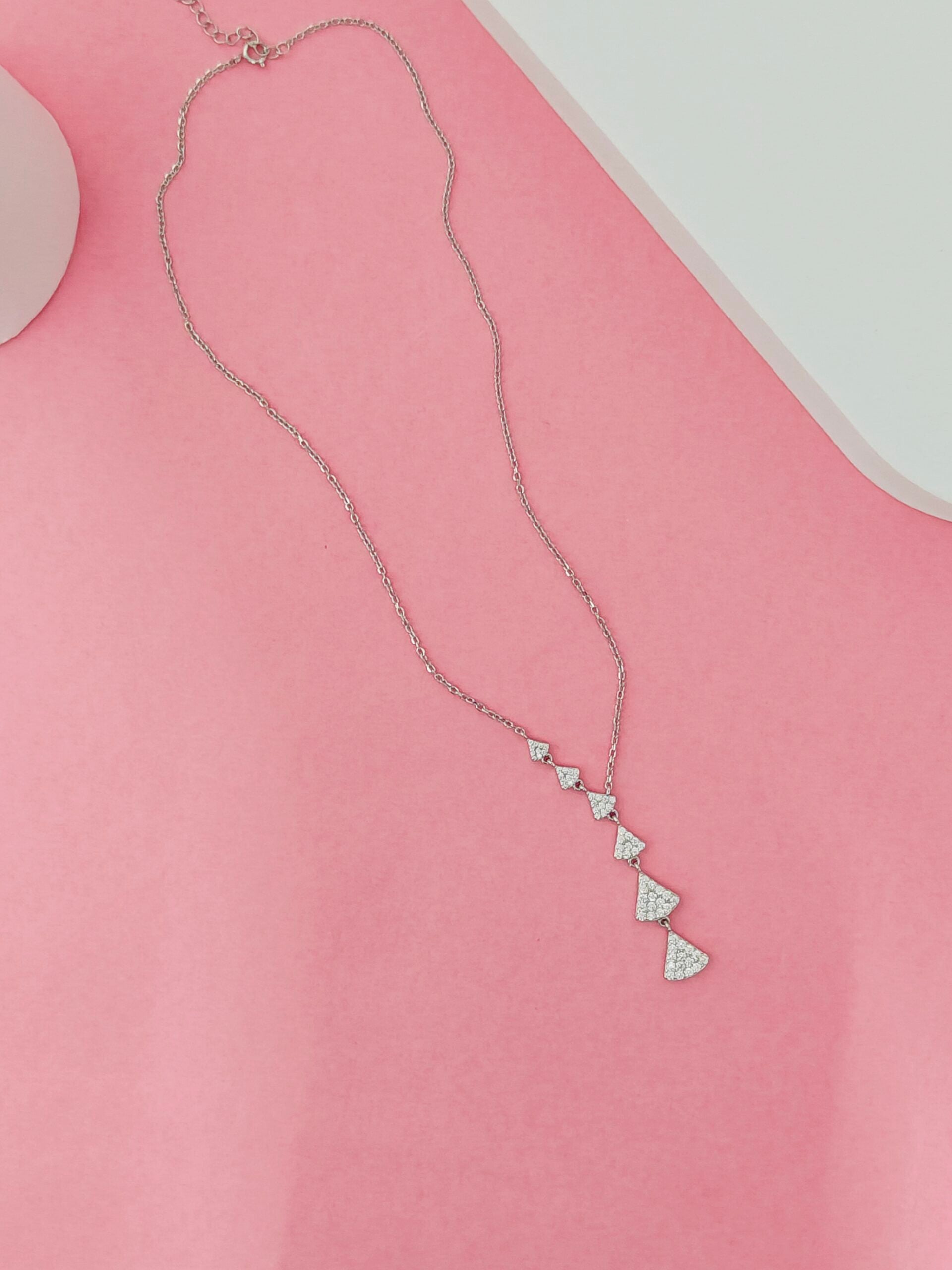 Necklace with triangular pendants on a pink surface